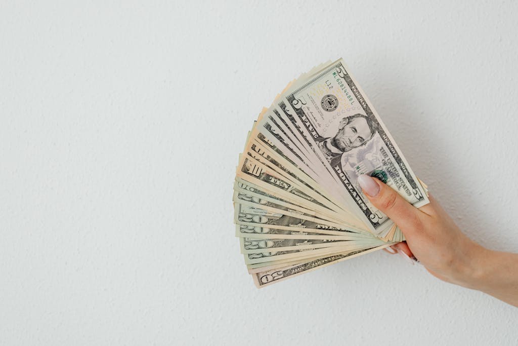 A hand holding an array of US dollar bills, fanned out against a plain white background.