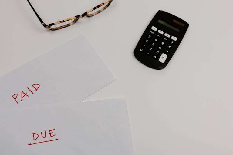 Top view of financial papers labeled 'Paid' and 'Due' beside a calculator and glasses.